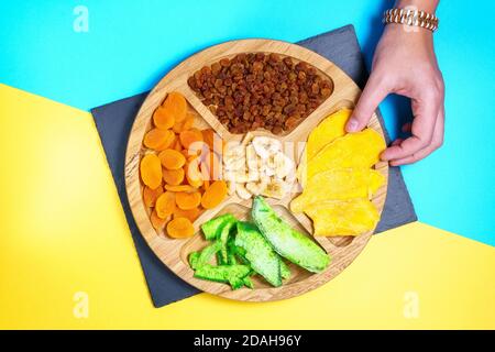 Mischung aus getrockneten Früchten auf TU Bischvat Mandala blau, gelber Hintergrund flach legen. Mango, Rosinen, Papaya, Bananen, getrocknete Aprikosen Stockfoto