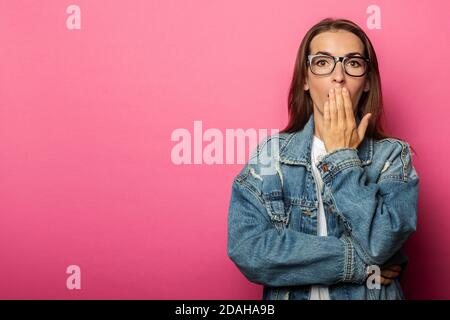 Junge Frau in Gläsern gähnt über ihren Mund mit Handfläche auf rosa Hintergrund. Stockfoto