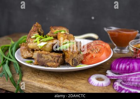 Gegrillte Fettschweinerippen auf einem Knochen serviert auf einem Teller mit Gemüse. Geröstetes Grillfleisch auf dunklem Hintergrund. Stockfoto