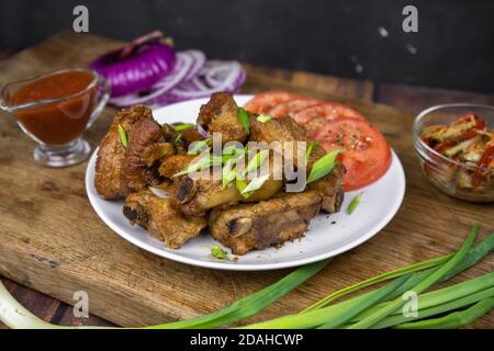 Gegrillte Fettschweinerippen auf einem Knochen serviert auf einem Teller mit Gemüse. Geröstetes Grillfleisch auf dunklem Hintergrund. Stockfoto