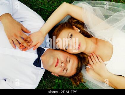 Nahaufnahme Porträt von frisch verheirateten Paar auf Gras liegen und Hände halten. Stockfoto