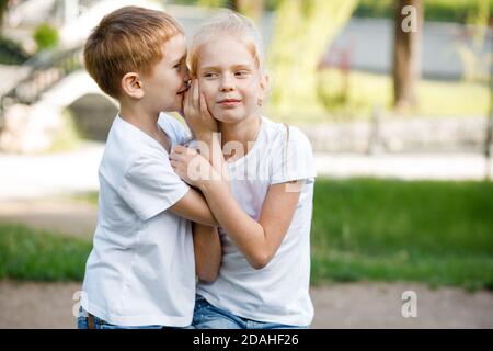 Der Junge flüstert dem Mädchen ein Geheimnis ins Ohr. Kinder für einen Spaziergang im Park. Stockfoto