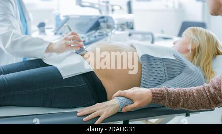 Im Krankenhaus, Nahaufnahme des Arztes führt Ultraschall Sonogramm Verfahren, schwangere Frau auf dem Bett liegen. Beweglicher Schwinger Für Geburtshelfer Stockfoto