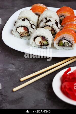 Sushi rollt auf einem weißen Teller auf schwarzem Hintergrund Mit eingelegtem Ingwer Stockfoto