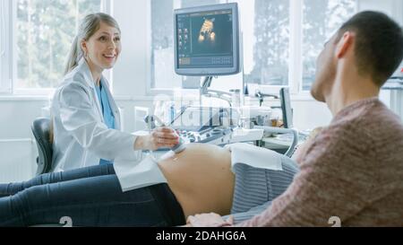 Im Krankenhaus, schwangere Frau bekommen Ultraschall-Sonogramm-Scan, Geburtshilfe erklärt ihr und ihrem unterstützenden Ehemann Verfahren. Frohe Familie Stockfoto