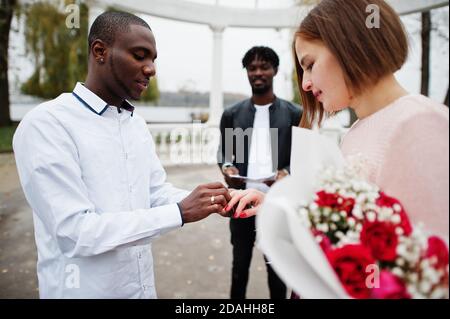 Hochzeit Verlobungszeremonie mit Pastor. Multiethnische Paare stellen sich gegenseitig klingeln. Beziehungen von afrikanischem Mann und weißer europäerin. Stockfoto
