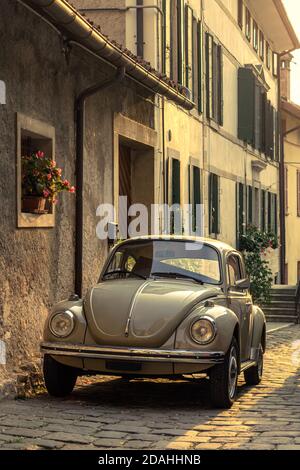 Volkswagen Käfer Auto geparkt zwischen den Gebäuden der Altstadt, beleuchtet von der untergehenden Sonne. Feltre, Belluno, Italien Stockfoto