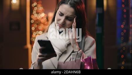 Gestresste Frau, die Weihnachtseinkäufe in den Straßen der Stadt macht, hat sie schlimme Kopfschmerzen Stockfoto