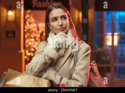 Schöne junge Frau tun Weihnachtseinkäufe in der Straße und Denken mit der Hand am Kinn Stockfoto