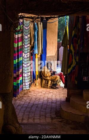 Ouarzazate; Marokko - 25. DEZEMBER 2019: afrikanischer Mann verkauft typische Berberartikel und Teppich im Souk der zentralen Medina Stockfoto