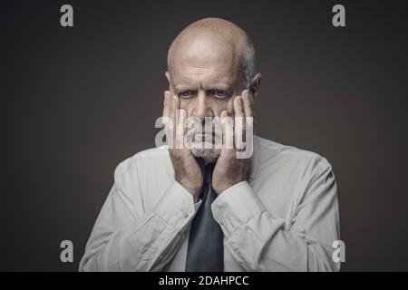 Panisch Geschäftsmann mit Kopf in den Händen, er ist erschrocken und besorgt Stockfoto