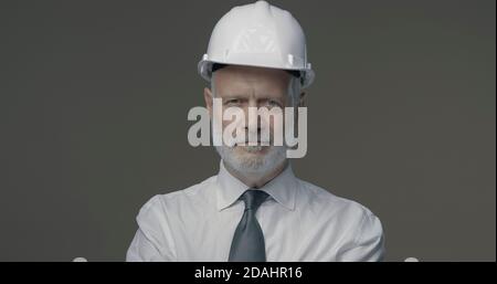 Selbstbewusster Geschäftsmann und Ingenieur, der mit einem Schutzhelm posiert, lächelt er vor der Kamera Stockfoto