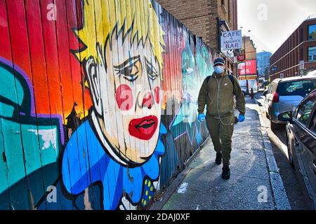 GROSSBRITANNIEN / England / London / EIN Mann mit Gesichtsmaske geht an Graffiti vorbei, das Premierminister Boris Johnson als Clown zeigt, nahe der Brick Lane. Stockfoto