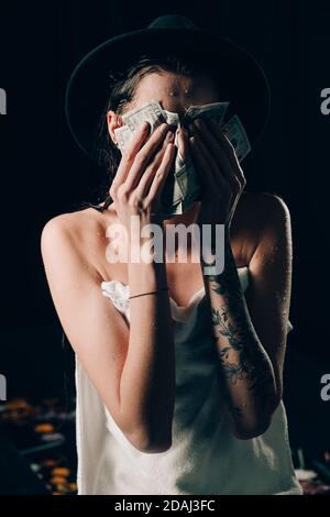 Schöne Frau in einem Handtuch und schwarzen Hut hält Dollar und Sorge für Not, Weinen wütend und Angst. Trauriger Ausdruck. Stockfoto