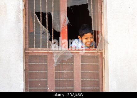 Sur, Oman - 15. Februar 2020: Unidentifizierter omanischer glücklicher Junge lächelt durch das alte Fenster seines alten Hauses in Sur, der Stadt des Sultanats von Oman. Stockfoto