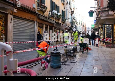 Die Arbeiter in hellen Schutzwesten reparieren Pflasterplatten auf der Stadtstraße. Venedig von Italien. Stockfoto