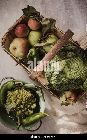 Korb gefüllt mit Äpfeln und ein wirsing-Kohl und ein Schüssel mit Romanesco Brokkoli und Chilischoten Stockfoto