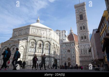 Die Menschen gehen vor einem mittelalterlichen religiösen Gebäude des Baptisteriums von San Giovanni (1059-1129) am Domplatz (Piazza del Duomo). Stockfoto