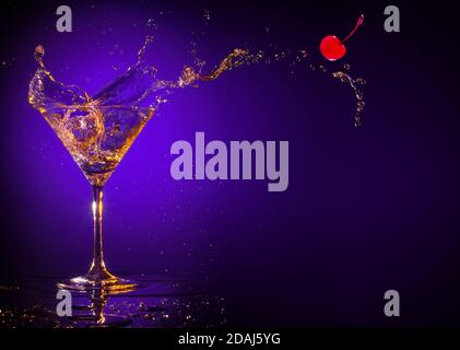 Rote Kirsche spritzt aus einem martini-Glas auf einem Violetter Hintergrund Stockfoto