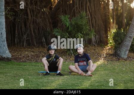 Nette Brüder sitzen und posieren auf ihren Skateboards im Sommer Stockfoto