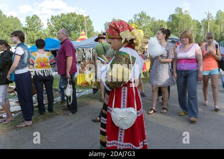 Mädchen in Volkstracht steht und schaut auf ein Handy in der Menge während der jährlichen Intl Festival of Music and Crafts World of Sibirian. Stockfoto