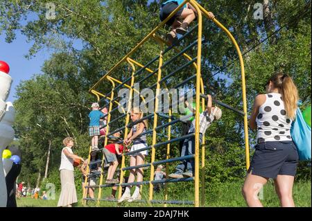 Kinder spielen an einem sonnigen Sommertag auf der Sporttreppe des Spielplatzes unter Aufsicht ihrer Eltern. Stockfoto