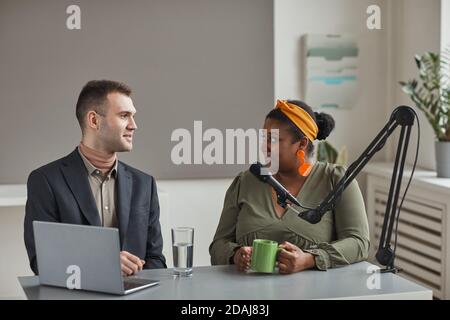 Zwei Geschäftsleute sitzen am Tisch mit Laptop und Mikrofon und haben ein Interview im Radio Stockfoto