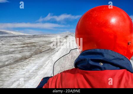 Mann mit rotem Helm und Jacke von hinten gesehen Auf einem Schneemobil auf einem Gletscher in der Sonne Stockfoto