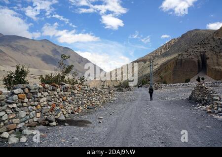 Touristen wandern entlang einer unbefestigten Straße entlang eines Steinzauns im Himalaya, auf dem Weg nach Upper Mustang in Nepal. Stockfoto