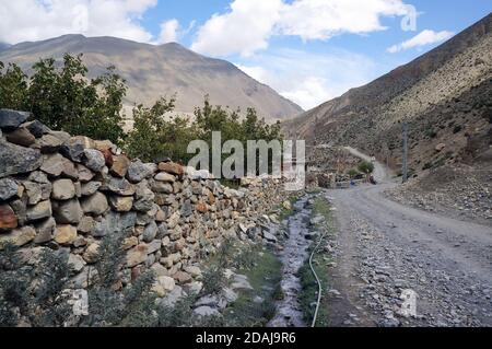 Eine unbefestigte Straße verläuft entlang eines Steinzauns im Himalaya, auf dem Weg nach Upper Mustang in Nepal. Stockfoto