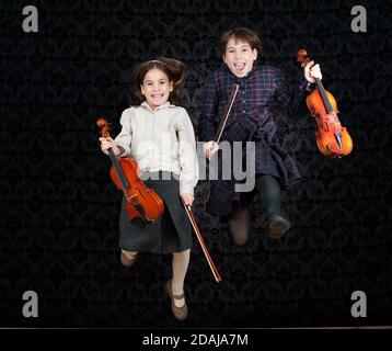 Zwei Mädchen mit Geigen springen auf einem Vintage-Hintergrund Stockfoto