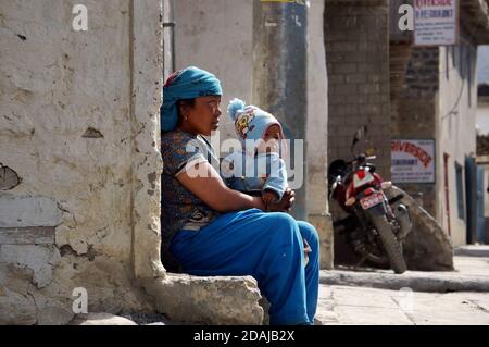 Eine nicht identifizierte nepalesische Frau mit einem kleinen Kind auf den Knien sitzt an der Wand eines Hauses in der Jomsoma Street. Nepal. Stockfoto