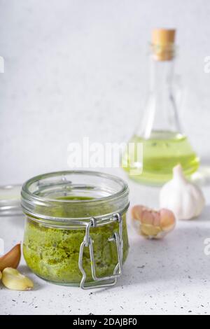 Selektiver Fokus. Basilikum und Käse Pesto Paste. In einem kleinen Glas. Auf hellem Hintergrund. Mit frischem Knoblauch und Öl Stockfoto