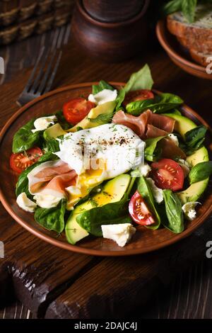 Eier Benedikt (pochiert) mit Parmaschinken, Scheiben Avocado, Tomaten und zarten Spinatblättern, gewürzt mit würzigem Olivenöl Stockfoto