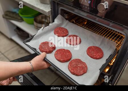 Weibliche Hände machen Fleischbällchen im Ofen. Amerikanische Fleischbällchen für Burger. Hausgemachte, gebratene Rinderpasteten. Stockfoto