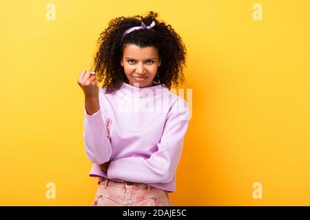 Unzufriedene afroamerikanische Frau mit geballter Faust auf gelb Stockfoto