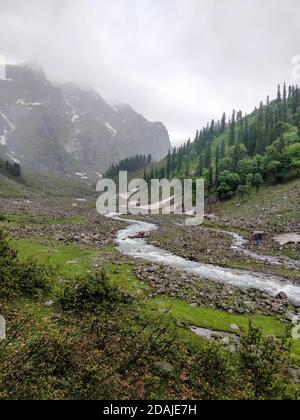 Schneepatches und Flussstrom, der durch Felsen in einem epischen indischen Himalaya Mountain Valley fließt. Stockfoto