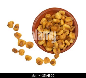 Draufsicht auf eine kleine Tonschale aus Bio-Maisnüssen mit mehreren Nüssen, die außerhalb der Schale isoliert auf weißem Hintergrund gestreut sind. Stockfoto