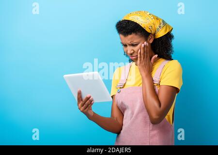 Verärgert afroamerikanische Frau im Kopftuch mit digitalen Tablet auf Blau Stockfoto