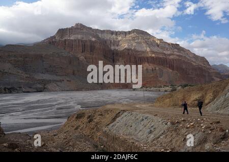 Touristen mit Trekkingstäbchen wandern entlang des Kali Gandaki Flusses vor der Kulisse der Chhusang Klippen. Trekking zum Oberen Mustang. Nepal. Stockfoto