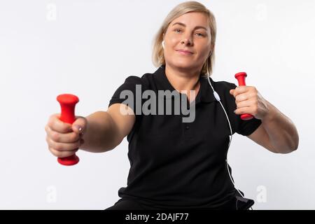 Ältere Frau Sport zu Hause mit Hanteln hören Sie die Musik mit Kopfhörern. Fitnesskonzept während einer Pandemie. Foto auf weißem Hintergrund. Stockfoto
