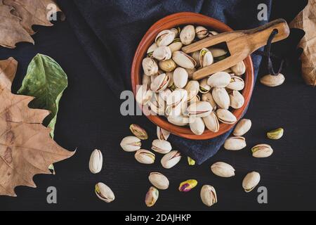 Pistazien auf schwarzem Holzbrett und Herbstblättern Stockfoto