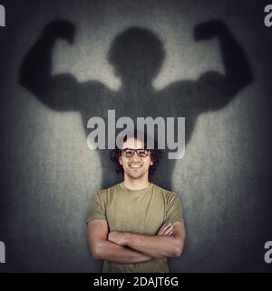 Selbstbewusste Schatten des jungen Mannes verwandelt sich in eine muskulöse Person an der Wand als Metapher für innere Kraft. Motivierter Kerl vorstellen Flexing großen Bizeps als Stockfoto