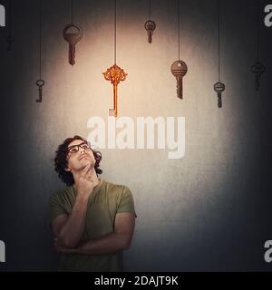 Nachdenklicher junger Mann hält die Hand unter dem Kinn, nachdenkliche Geste, fokussiert nach oben schauen, einen hängenden goldenen Schlüssel anstelle von mehreren anderen wählen. Richtige Wahl Stockfoto