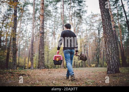 Thema ist der Tod des Haustieres. Rückansicht des Mannes, der entlang Waldweg geht und Schaufel in einer Hand zum Graben Grab trägt, und in anderen Transportbox mit Stockfoto