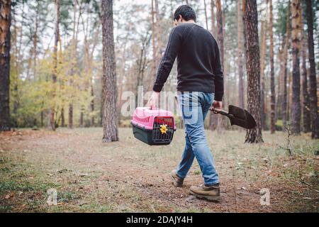 Thema ist der Tod des Haustieres. Rückansicht des Mannes, der entlang Waldweg geht und Schaufel in einer Hand zum Graben Grab trägt, und in anderen Transportbox mit Stockfoto