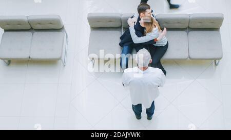 High Angle Shot im Krankenhaus, Junges Paar sitzt in der Lobby und umarmt. Sie erhalten Testergebnisse mit guten Nachrichten von ihrem Arzt. Glücklich Stockfoto