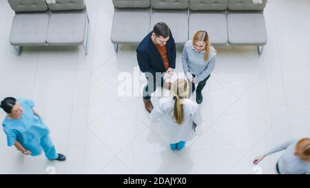 High Angle Shot in der Krankenhauslobby, Young Couple Talks trifft sich mit Ärztin Arzt Krankenschwester, Sie haben Diskussion. Neues, Sauberes, Modernes Krankenhaus Stockfoto