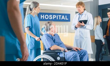 In der Krankenhauslobby schiebt die Krankenschwester ältere Patienten in den Rollstuhl, der Arzt spricht mit ihnen, während er einen Tablet-Computer verwendet. Sauber, neues Krankenhaus mit Stockfoto