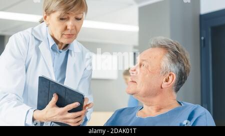 Im Krankenhaus zeigt eine Ärztin einem älteren Patienten einen Tablet-Computer und erklärt seinen Zustand. Modernes Krankenhaus mit bester Betreuung. Stockfoto